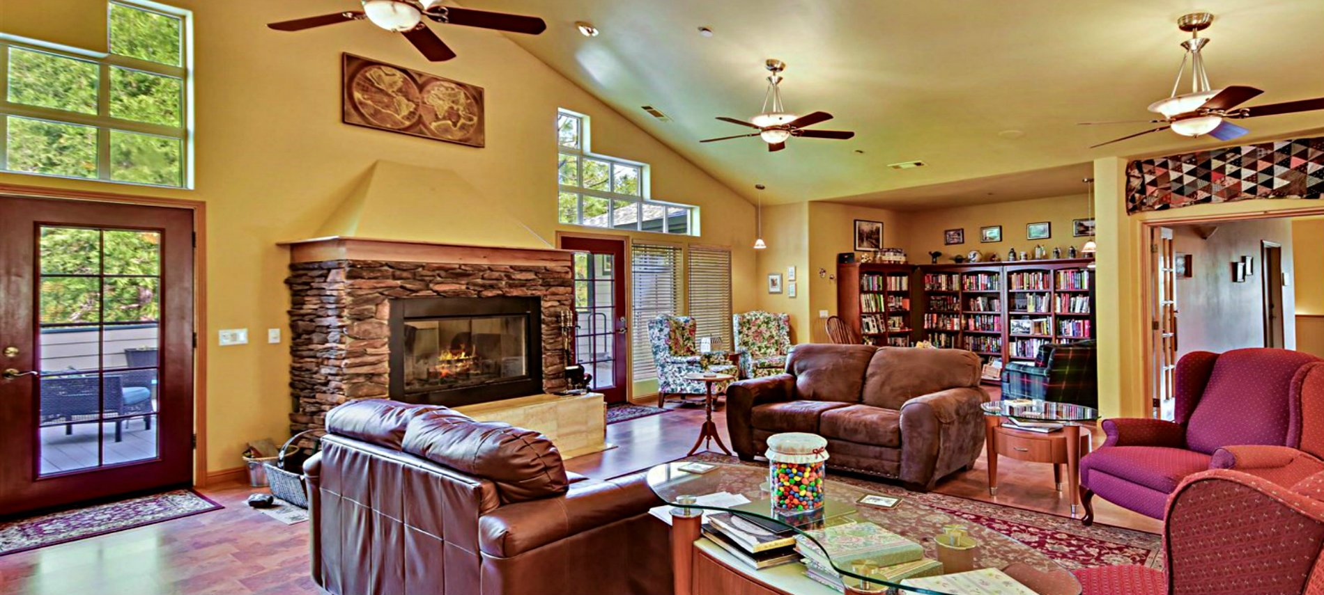 A large sitting room with brown sofas, red chairs, bookcases, a fireplace, ceiling fans and yellow walls. 